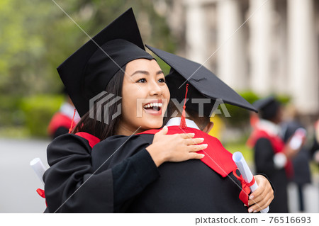 Cheerful asian lady hugging her boyfriend while graduation ceremony 76516693