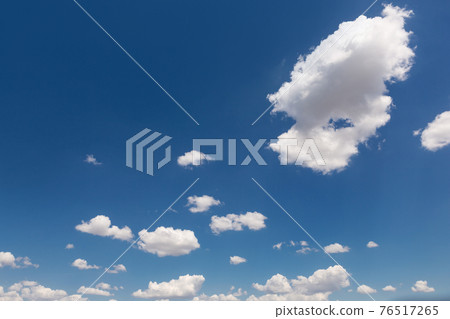 a lot of clouds in a blue sky, arranged randomly, one cloud is much larger than others 76517265