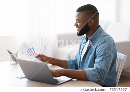 Remote Business. Black Entrepreneur Working With Papers And Laptop At Home Office Remote Business. Black Entrepreneur Working With Papers And Laptop At Home Office 76517367