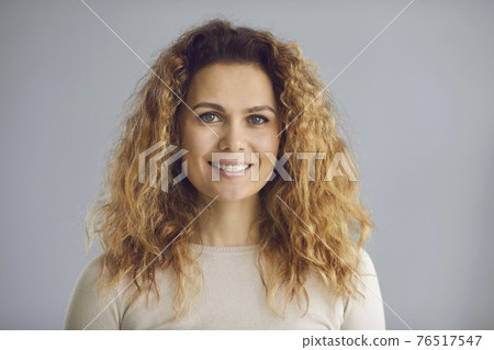Studio head shot of a happy woman with long wavy hair and a friendly white smile Studio head shot of a happy woman with long wavy hair and a friendly white smile 76517547