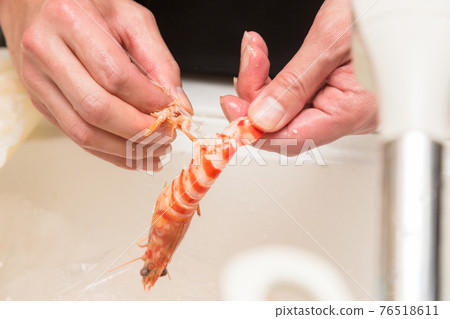 Hands in front of the board to peel the prawns 76518611