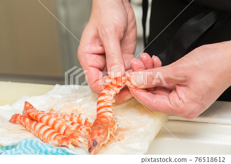 Hands in front of the board to peel the prawns 76518612