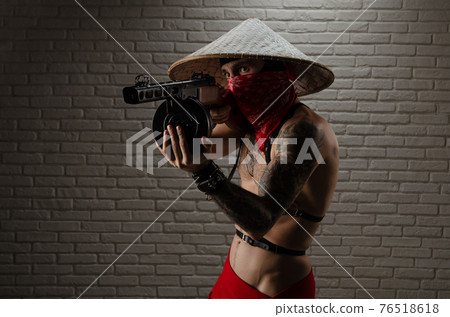 man in an Asian triangular hat with tattoos and a PPSh-41 airsoft gun and against the background of a brick wall 76518618