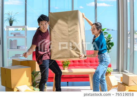 young asian couple smiling and enjoy when they carrying big cardboard box while relocation into new home on moving day, celebrating moving to new home concept 76519058