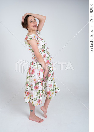 Studio portrait of cheerful young pregnant woman in summer dress on white gray background, happy pregnancy concept 76519298