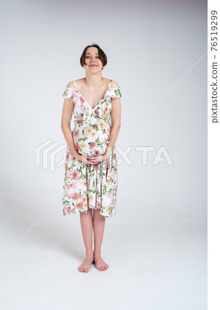 Studio portrait of cheerful young pregnant woman in summer dress on white gray background, happy pregnancy concept 76519299