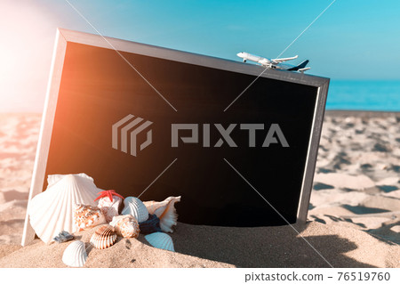 Summer time. Globe, seashell, airplane and starfish near black desk on sea beach in sunny day. Exotic tropical beach with copy space. 76519760