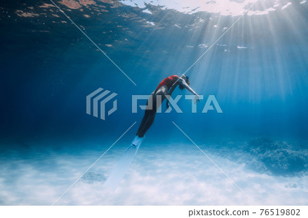 Woman freediver in swimsuit with fins glides underwater over sand in tropical ocean. 76519802