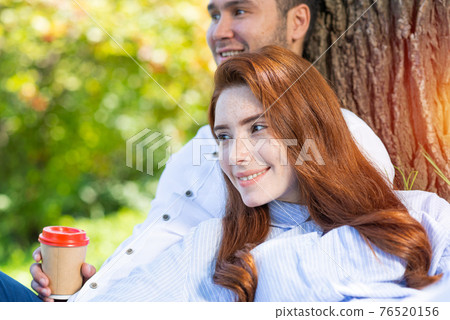 Young couple relaxing with coffee under tree 76520156