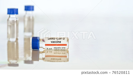 Coronavirus Covid 19 vaccine concept - small glass vials with blue caps on white table, closeup detail (own sticker design with dummy data - not real product) 76520811