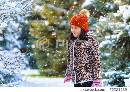 child girl throws up snow and playing in the winter forest, bright snowy fir trees, beautiful nature 76521389
