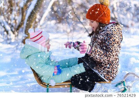 children sitting on sledge in the winter forest and playing, bright sunlight and shadows on the snow, beautiful nature 76521429