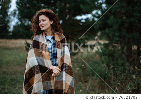 Attractive girl wrapped in a checkered plaid on a forest and field background 76521702