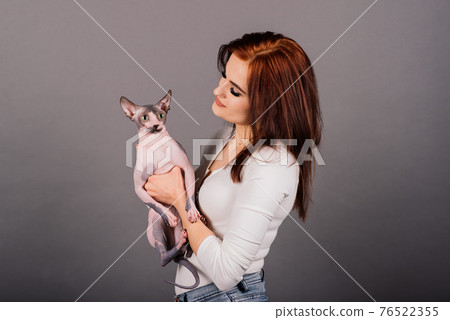 Gorgeous brunette woman smiling, holding Sphynx kitten, posing on grey and yellow studio background. Gorgeous brunette woman smiling, holding Sphynx kitten, posing on grey and yellow studio background. 76522355