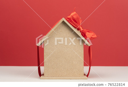 model of a wooden house tied with a red silk ribbon on a red background, concept of real estate purchase 76522814