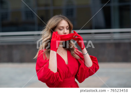Young woman in red dress and gloves puts on medical facemask 76523458
