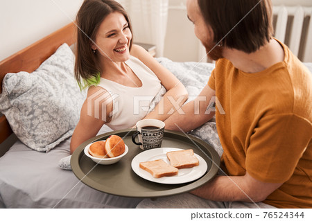 Man bringing breakfast at bed to his loving woman Man bringing breakfast at bed to his loving woman 76524344