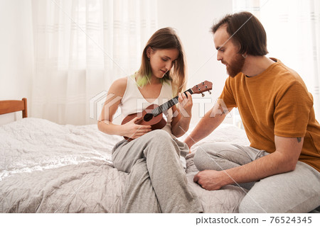 Couple sitting at the sofa and learning how to play at the ukulele Couple sitting at the sofa and learning how to play at the ukulele 76524345