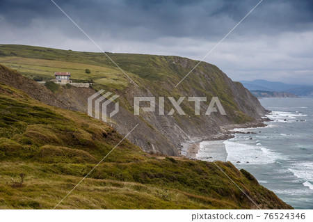 Scenic view over green hills, the lighthouse and ocean, waves hitting the rocks 76524346