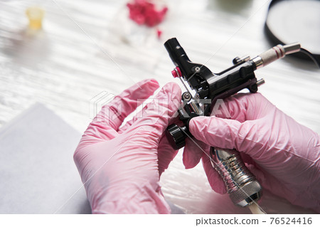 Artist wearing protective pink medical gloves assembling a tattoo machine Artist wearing protective pink medical gloves assembling a tattoo machine 76524416