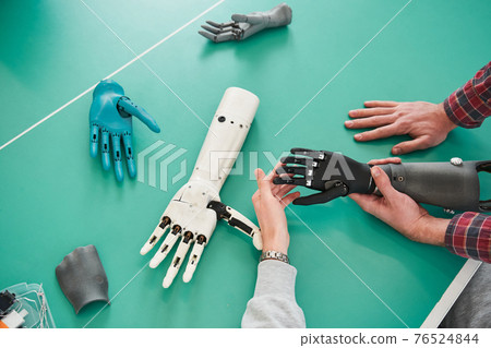 Young people holding prototype of mechanical hand in laboratory 76524844