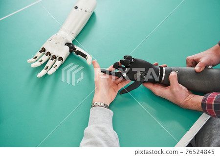 Two scientists examining mechanical hand in laboratory 76524845
