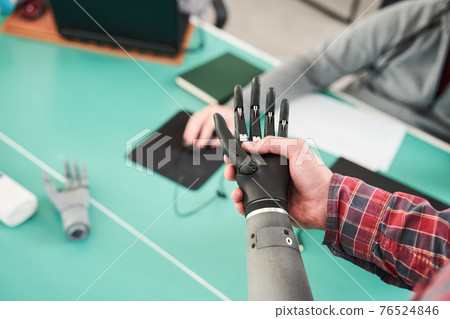 Prosthetist holding prosthetic hand while checking it for quality 76524846