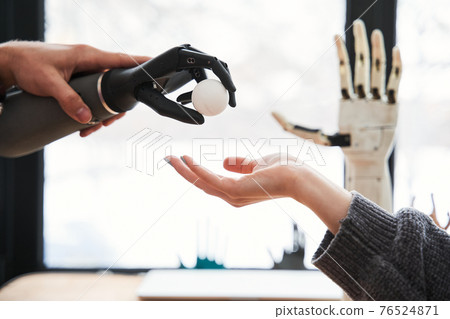 Engineer passes a tennis ball with the bionic hand to his female colleague 76524871