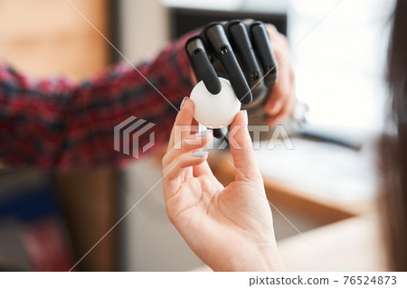 Bionic prosthesis hand holding tennis ball while female engineer testing it 76524873