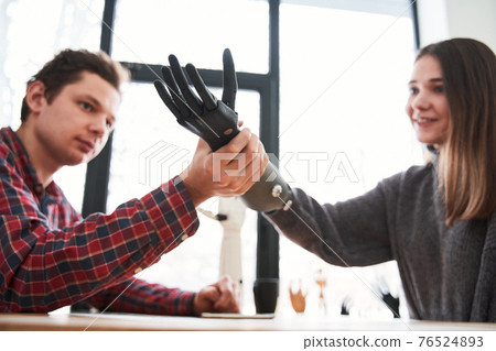 Portrait of the male engineer putting a prosthesis on a woman's hand 76524893