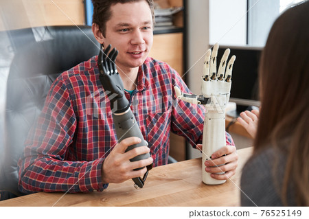Male engineer holding two examples of the prosthesis hands and discussing it 76525149