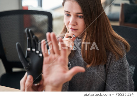 Woman looking critically and thoughtfully at the bionic prosthesis limb 76525154
