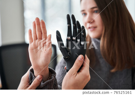 Woman comparing her hand with bionic prosthesis limb while sitting 76525161