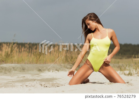Alluring model in yellow swimsuit on sandy shore 76528279