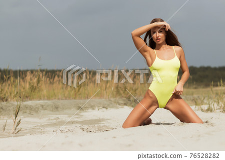 Alluring model in yellow swimsuit on sandy shore 76528282