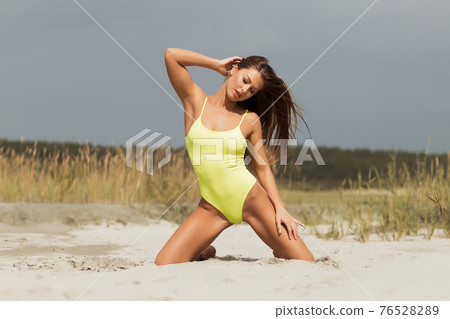 Alluring model in yellow swimsuit on sandy shore 76528289