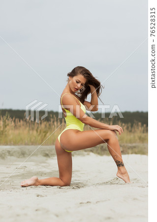 Erotic brunette in swimsuit posing on seashore 76528315