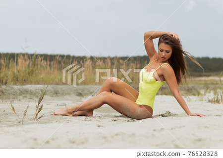 Sensual young woman in bright bodysuit lying on sand 76528328