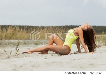 Sensual young woman in bright bodysuit lying on sand 76528329