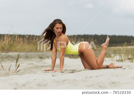 Erotic brunette in swimsuit posing on seashore 76528330