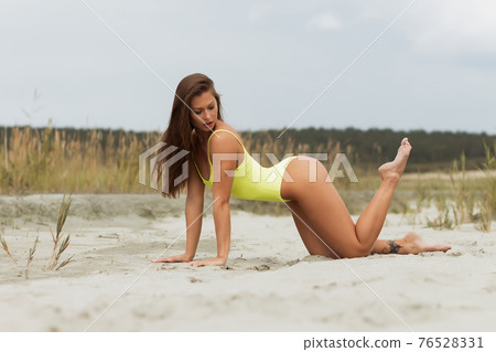 Erotic brunette in swimsuit posing on seashore 76528331