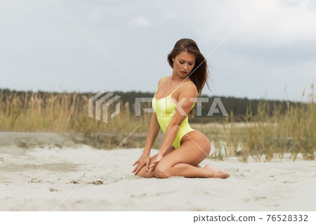 Erotic brunette in swimsuit posing on seashore 76528332