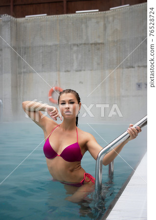 Slim woman standing on pool ladder 76528724