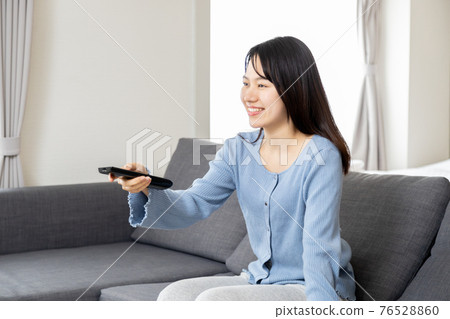 在沙發上操作遙控器的年輕女子 76528860