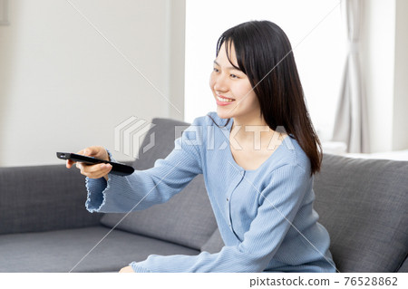 在沙發上操作遙控器的年輕女子 76528862