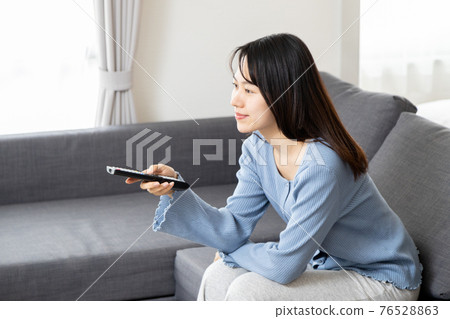 在沙發上操作遙控器的年輕女子 76528863