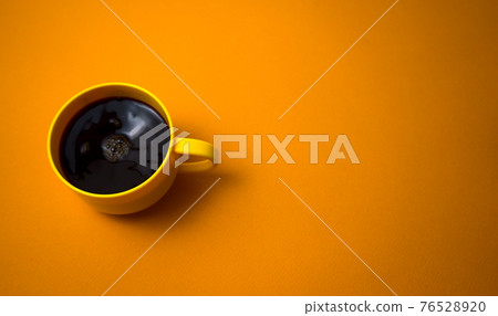 Yellow mug of stirring black coffee flat lay on dark yellow color background. Copy space for your text, image or message. Minimal, top view, horizontal image style. Off-center composition. 76528920