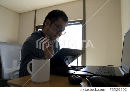 A man drawing an illustration with a pen tab 76529302