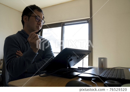 A man drawing an illustration with a pen tab 76529320