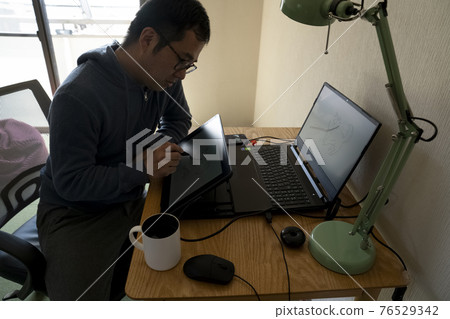 A man drawing an illustration with a pen tab 76529342